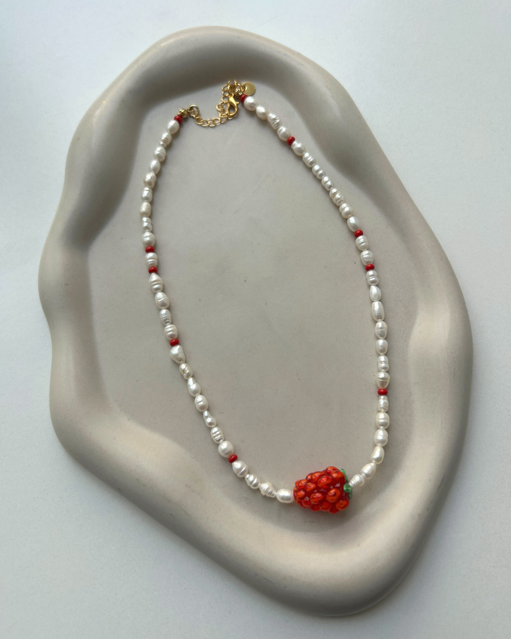 Perlenkette mit Himbeere auf grauem hintergrund