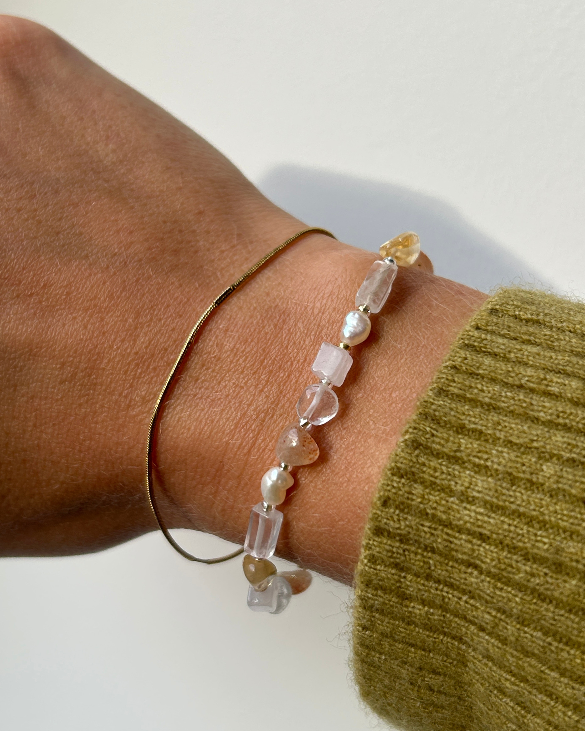 frau trägt zwei armbänder am handgelenk mit grünem pullover